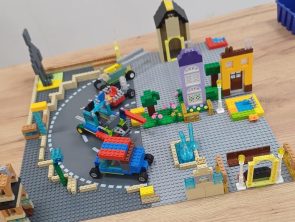 Makieta z klocków LEGO przedstawia fragmenty zabudowy, pas jezdni z autami