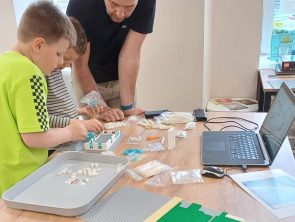 Uczestnicy warsztatów z LEGO budują makietę dworku Złotnickiego.