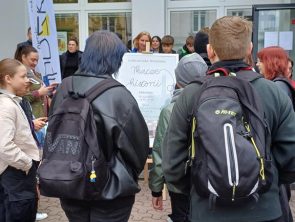 Uczestnicy gry terenowej przed budynkiem biblioteki słuchają wskazówek organizatora.