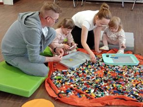 Rodzice wraz z dziećmi budują makietę z klocków LEGO.