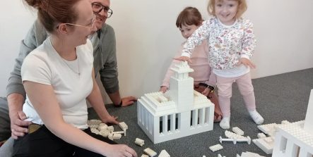 Rodzice wraz z dziećmi budują ratusz z klocków LEGO Duplo.