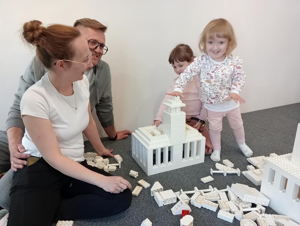 Rodzice wraz z dziećmi budują ratusz z klocków LEGO Duplo.
