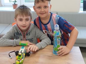 Chłopcy przy stole prezentują auto z klocków wykonane na warsztatach z robotyki