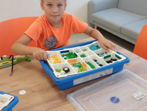 Dziewczynka siedzi przy stole i trzyma pudełko z klockami