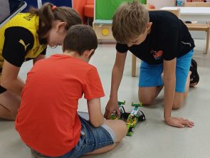 dwóch chłopców i dziewczynka klęczy nad modelami pojazdów