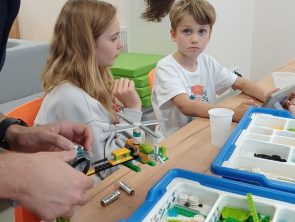 Prowadzący zajęcia i dzieci przy stołach budują modele pojazdów