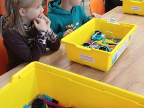 Dzieci przy stole wybierają klocki z pojemników