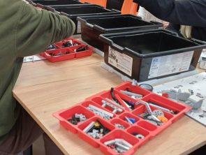 Uczestnicy warsztatów siedzą przy stole i wybierają klocki z pojemników