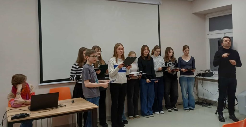 Dzieci stoją po ściana i czytają tekst z kartek