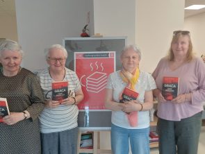 Na zdjęciu widać cztery kobiety stojące obok siebie. Każda z nich trzyma w dłoniach tę samą książkę – „Czarny poniedziałek" autorstwa Agnieszki Gracy. Za nimi stoi sztaluga z plakatem na którym jest napis „Dyskusyjny Klub Książki" oraz rysunkiem stosu książek.